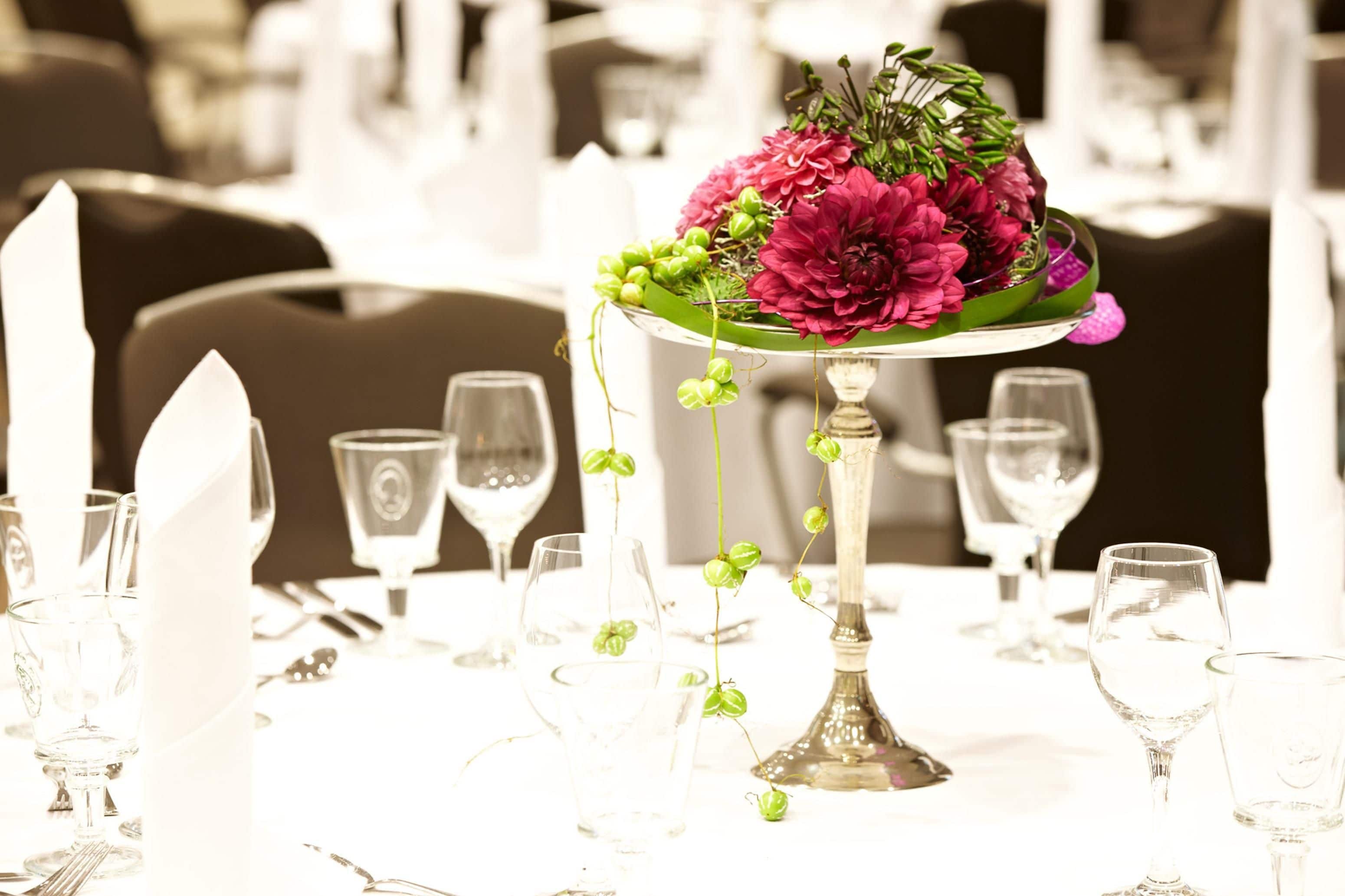 Een eettafel met een bloem- en groenarrangement als middelpunt, omringd door lege wijnglazen en bestek.