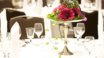 Una mesa de comedor con un centro de mesa de flores y follaje, rodeada de copas de vino vacías y cubiertos.