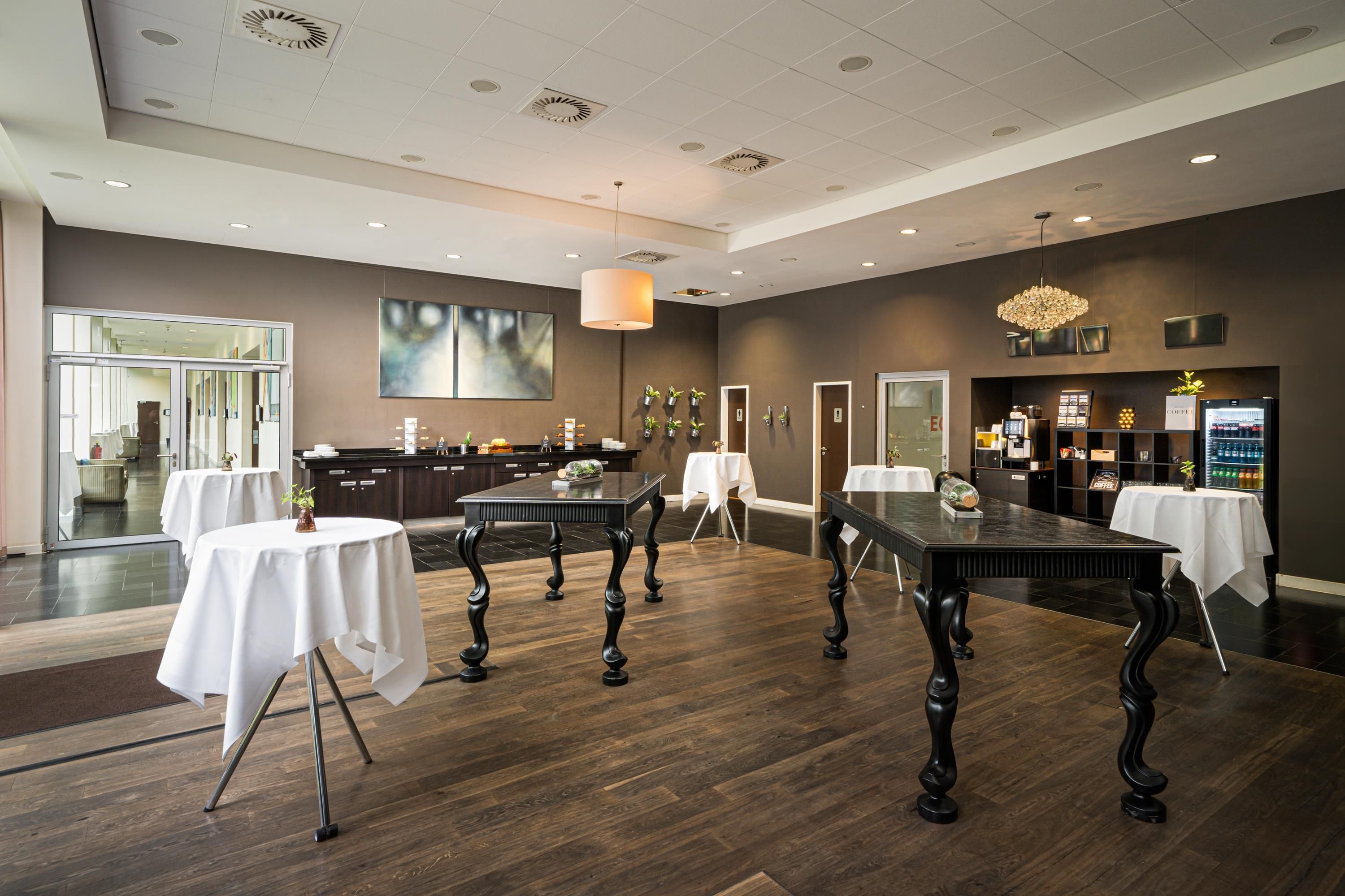 A spacious conference room with multiple tables, a large abstract painting, and a coffee station.