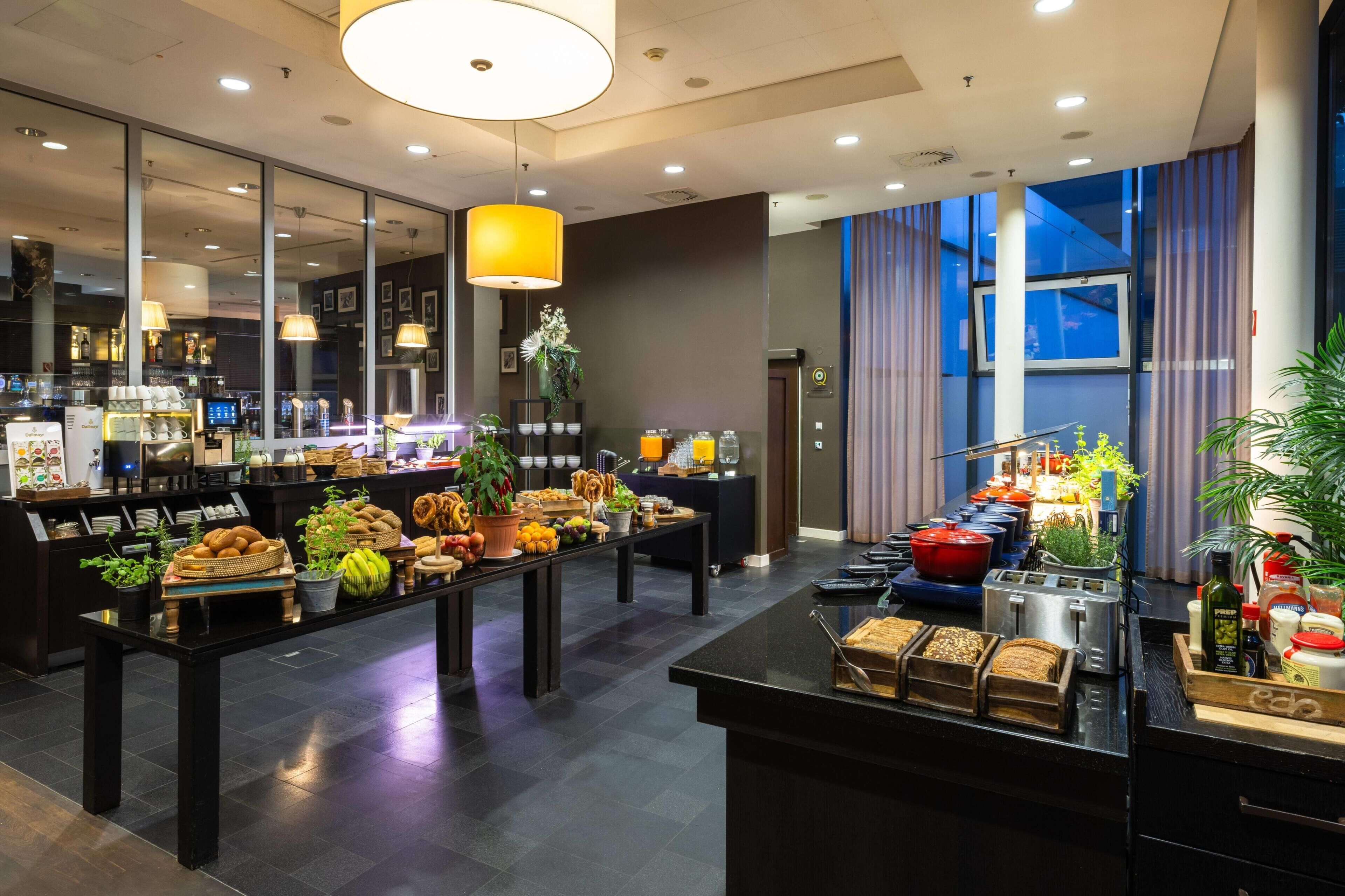 Eine moderne Hotelhalle mit einem Frühstücksbereich, der verschiedene Speisen sowie eine Kaffeestation bietet.