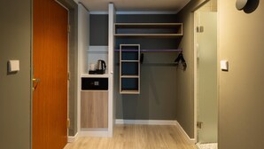 Una habitación compacta con puerta de madera, estanterías integradas, pequeña cocina y ducha.