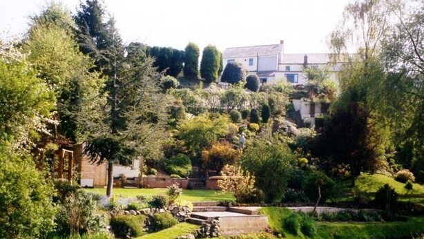 A garden with a pond, stone pathway, and a building in the background. - Brownhill House (Shrewsbury)