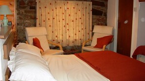 A bedroom with two beds, a stone wall, a wooden desk with a lamp, and two armchairs. - Brownhill House (Shrewsbury)