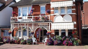 Un pub tradicional con un letrero que dice “The Chudleigh”. Cuenta con fachada de ladrillo, ventanas con marco blanco y un balcón con macetas colgantes de flores.