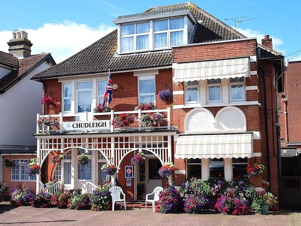 A traditional pub with a sign reading "The Chudleigh." It features a brick facade, white-framed windows, and a balcony with hanging flower baskets. - Chudleigh Hotel (Clacton-on-Sea)