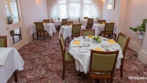 Un comedor con mesas redondas dispuestas para cuatro personas, cada una con manteles blancos, sillas y centros de mesa.