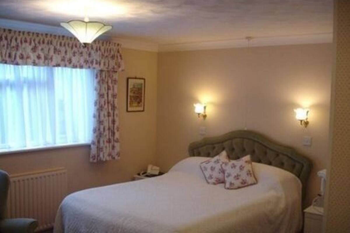 A bedroom with a large bed, two bedside lamps, a chair, and a window with curtains.