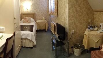 A compact hotel room with a bed, bedside table, a small desk with a chair, a TV, and a radiator.