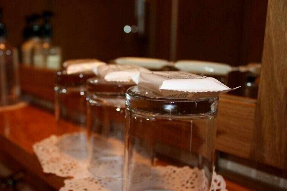 A row of clear glass jars with lids on a wooden surface, possibly containing food or beverages, with a lace doily underneath.