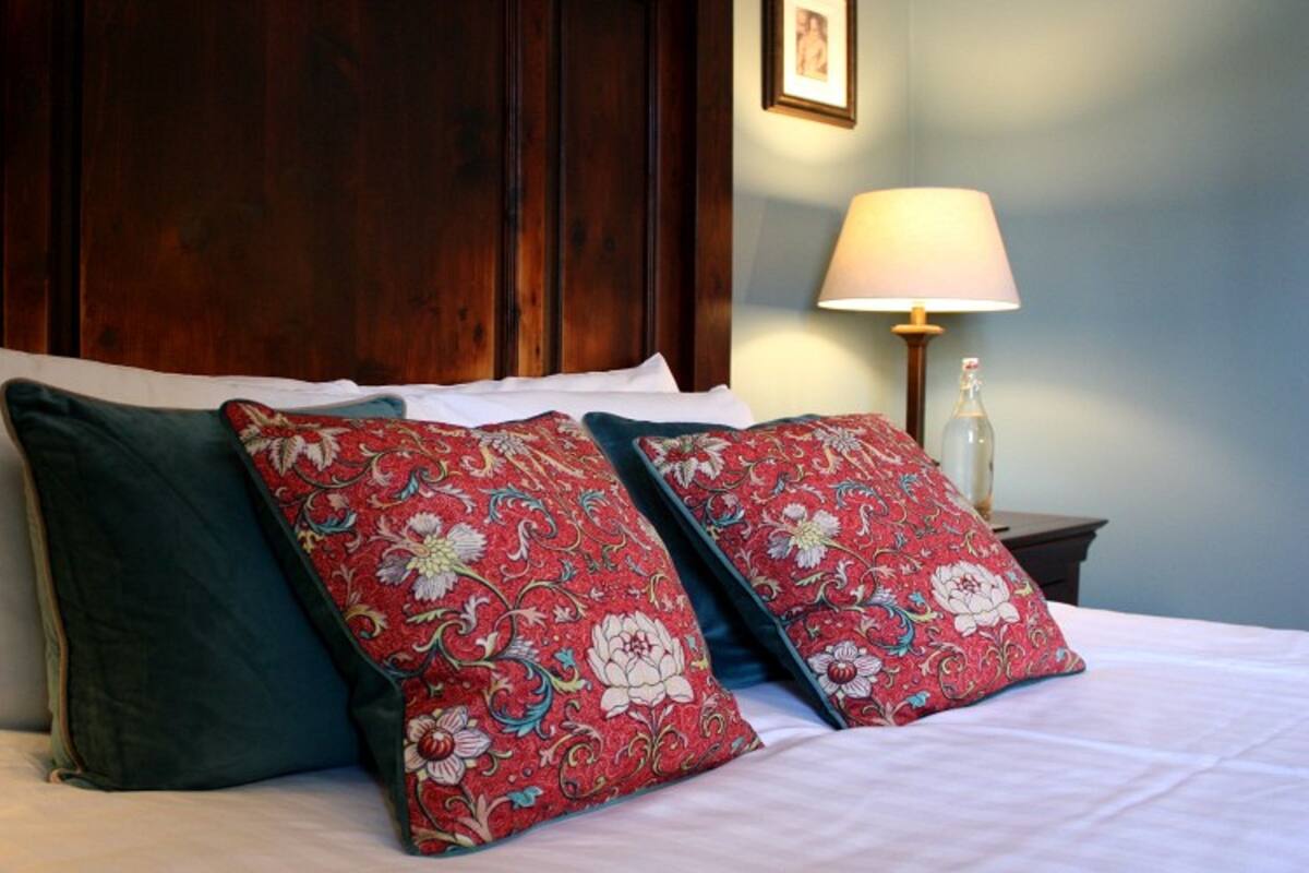A neatly made bed with white and green pillows, a wooden headboard, and a bedside table with a lamp and a bottle.