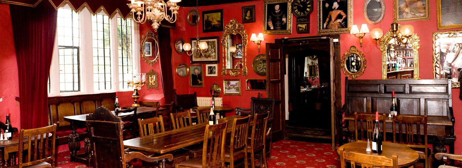 A room with a red wall, wooden furniture, and various framed pictures and mirrors.