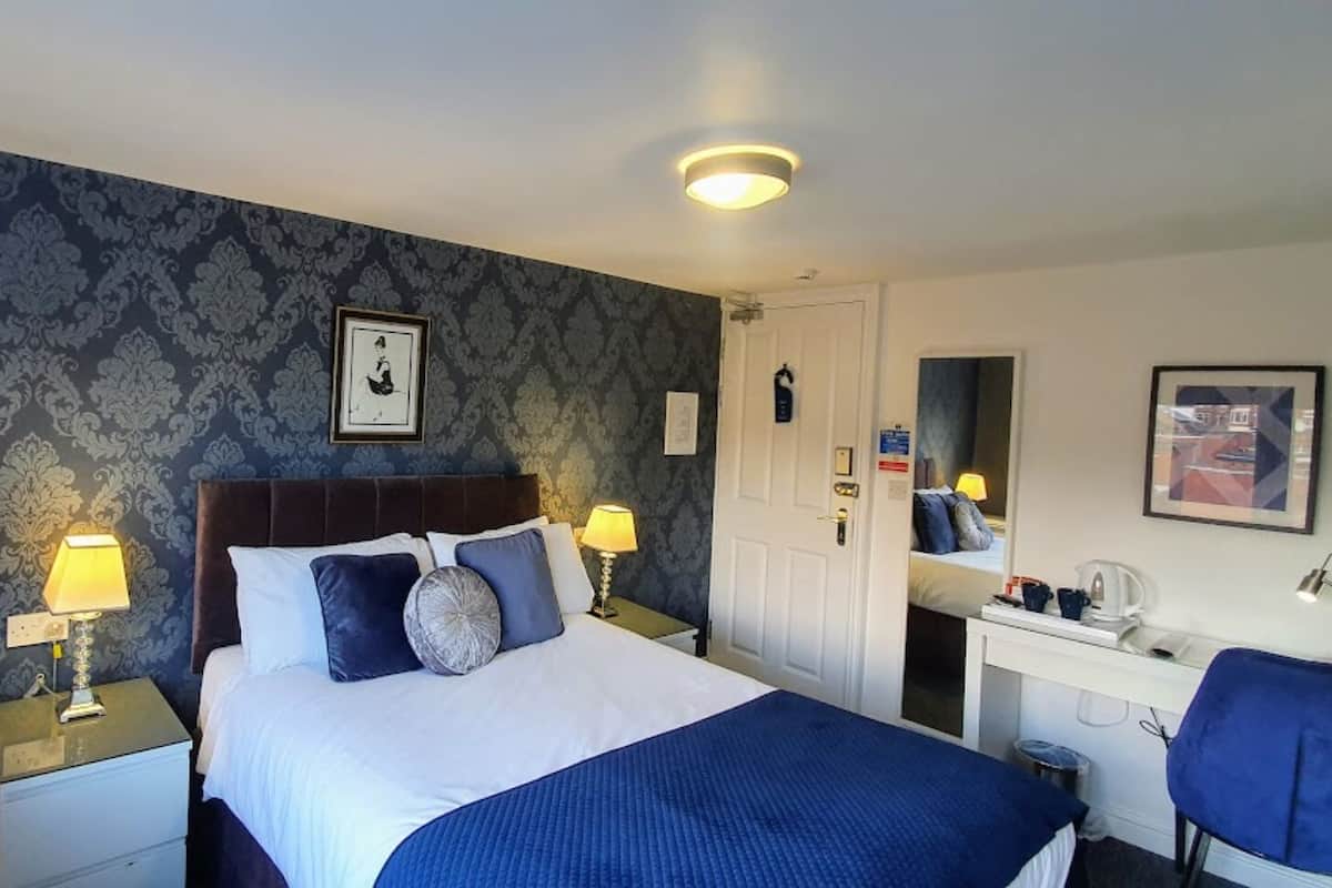 Habitación de hotel con una cama grande, dos mesitas de noche con lámparas, un escritorio con una silla, un espejo y una puerta.