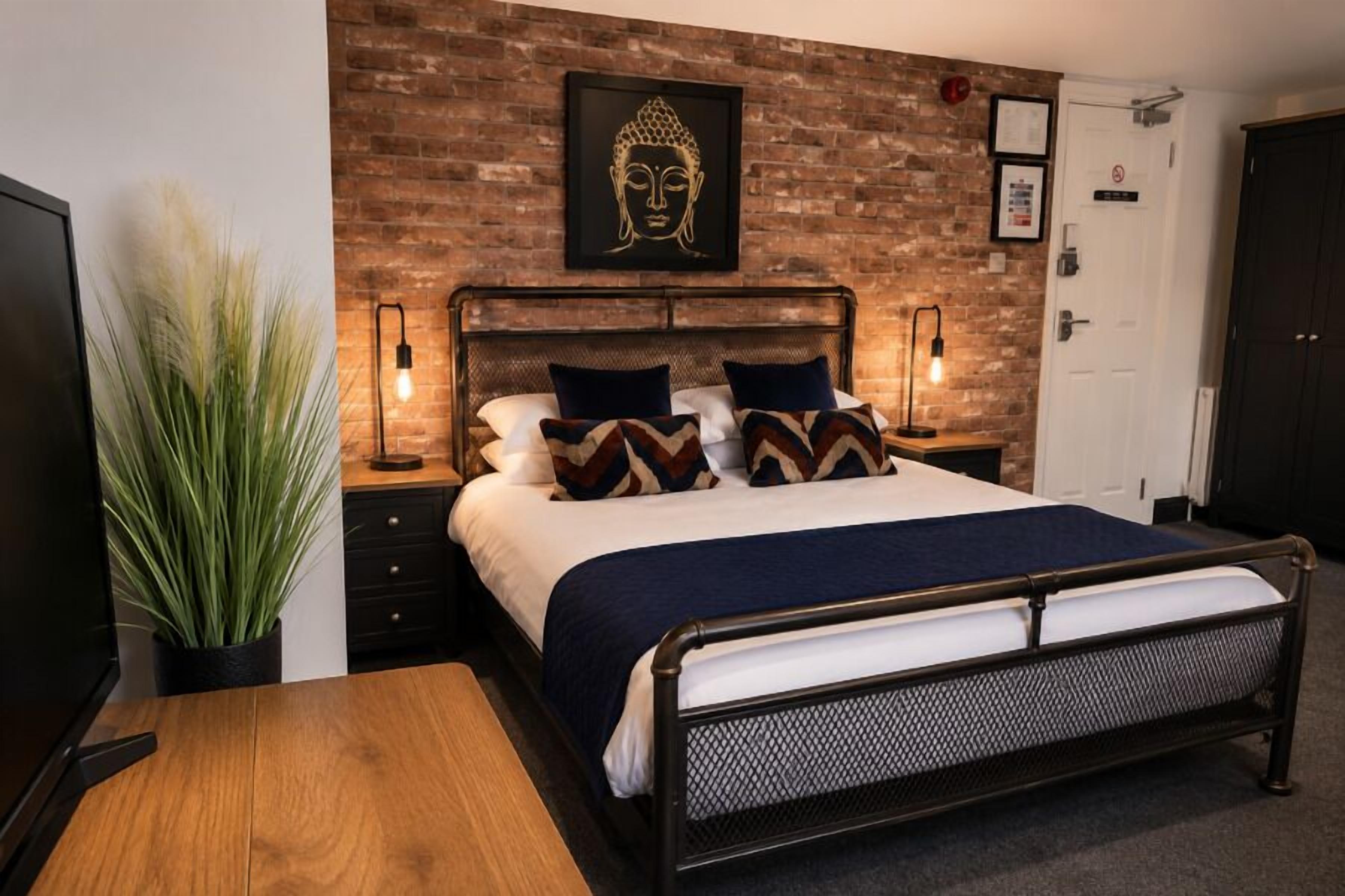 Een bed met een metalen frame, een bakstenen muur en een Boeddha-kunstwerk erboven.
