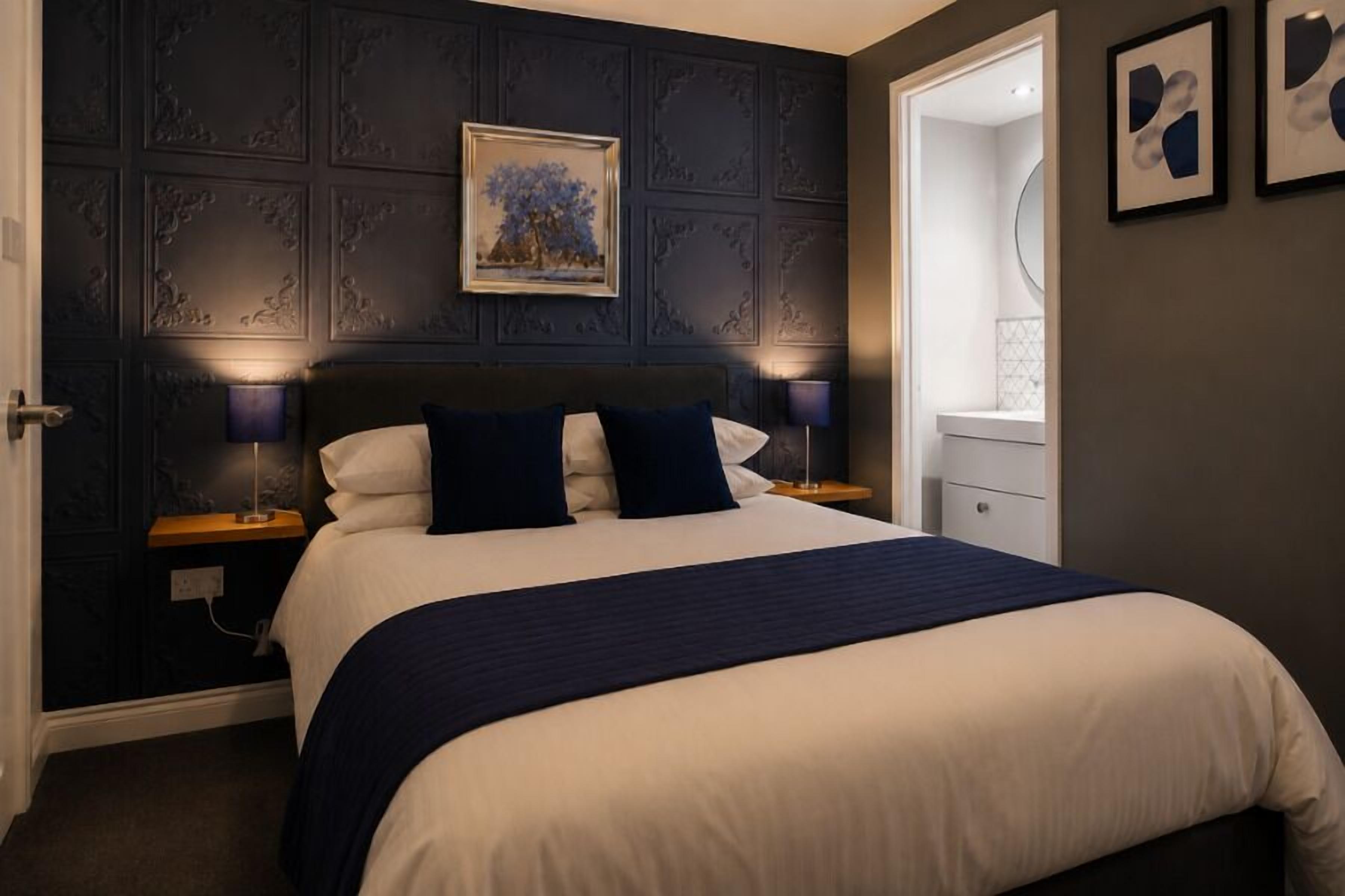 A neatly made bed with a dark headboard, two bedside tables with lamps, a framed picture above the bed, and a mirror on the wall.