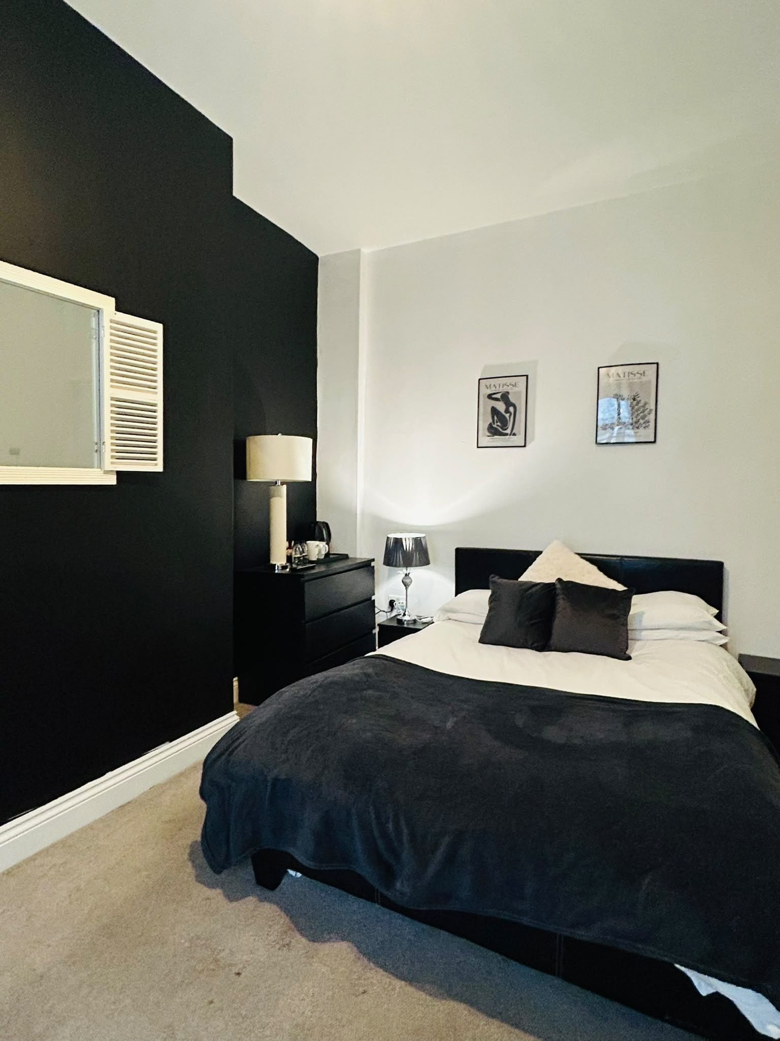 A bedroom with a black wall, a bed with white bedding, two bedside lamps, and two framed pictures on the wall.