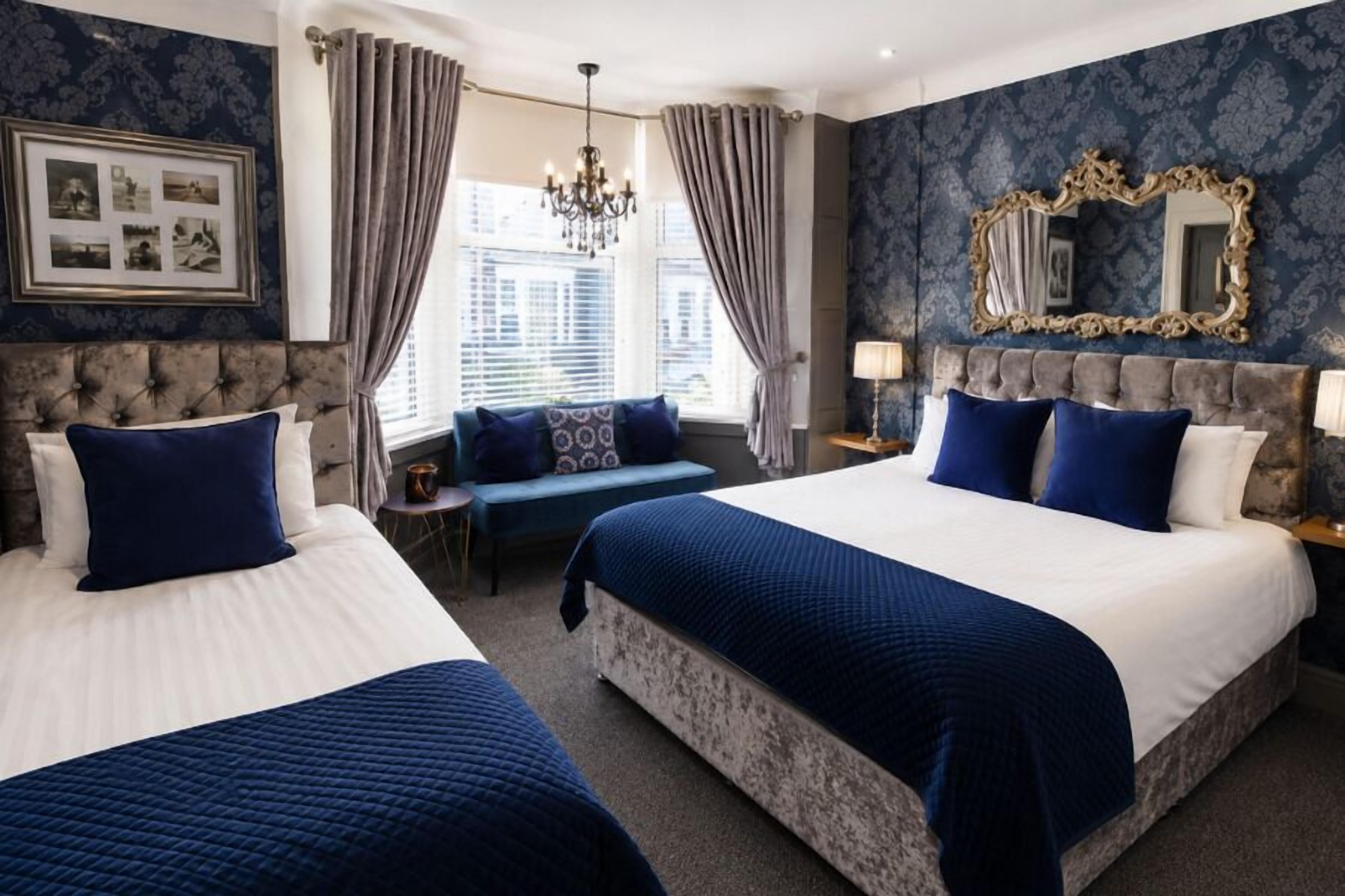 A hotel room with two beds, a chandelier, a large mirror, and a view of the city.