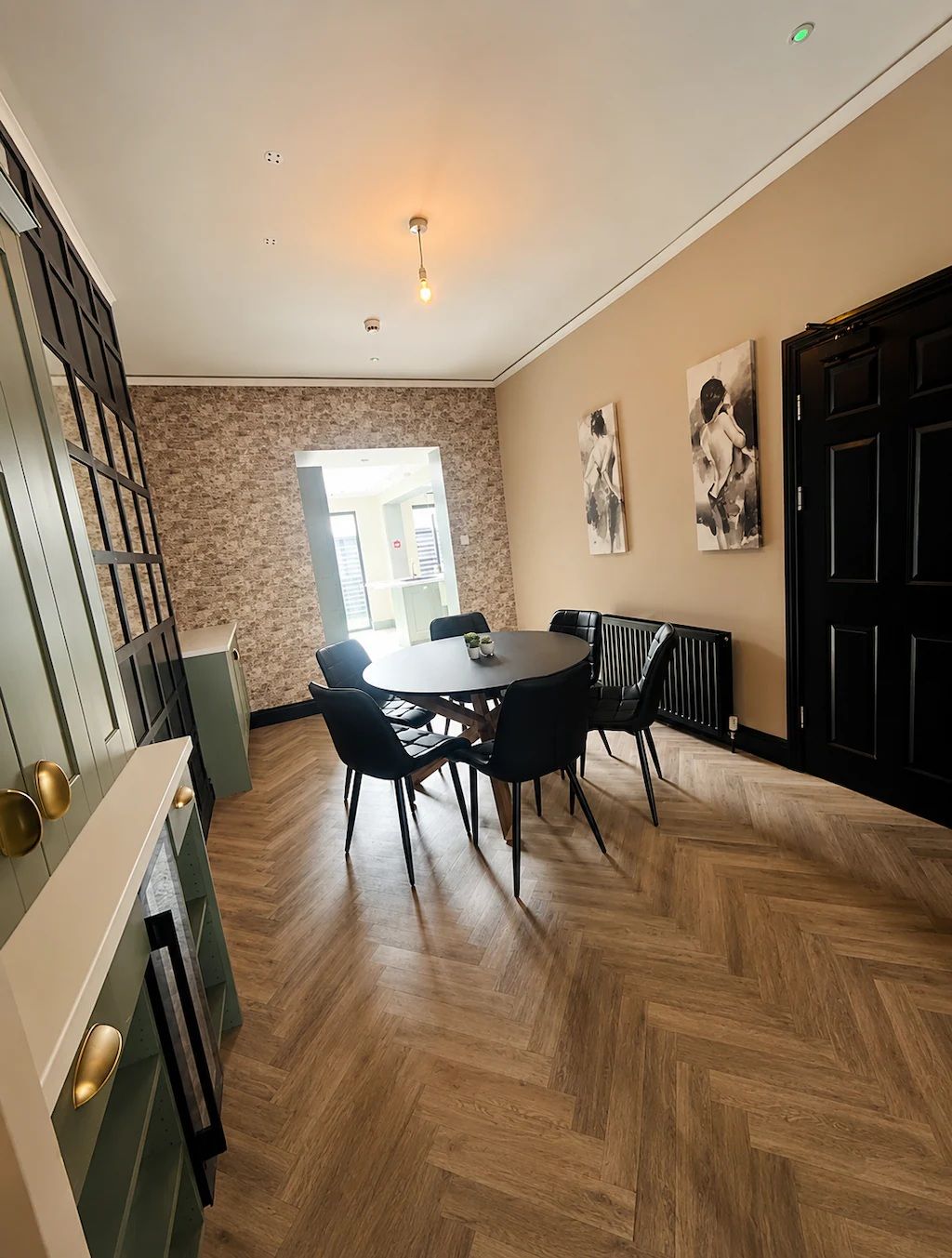 A dining area with a herringbone wood floor, a round table with chairs, and a black radiator.