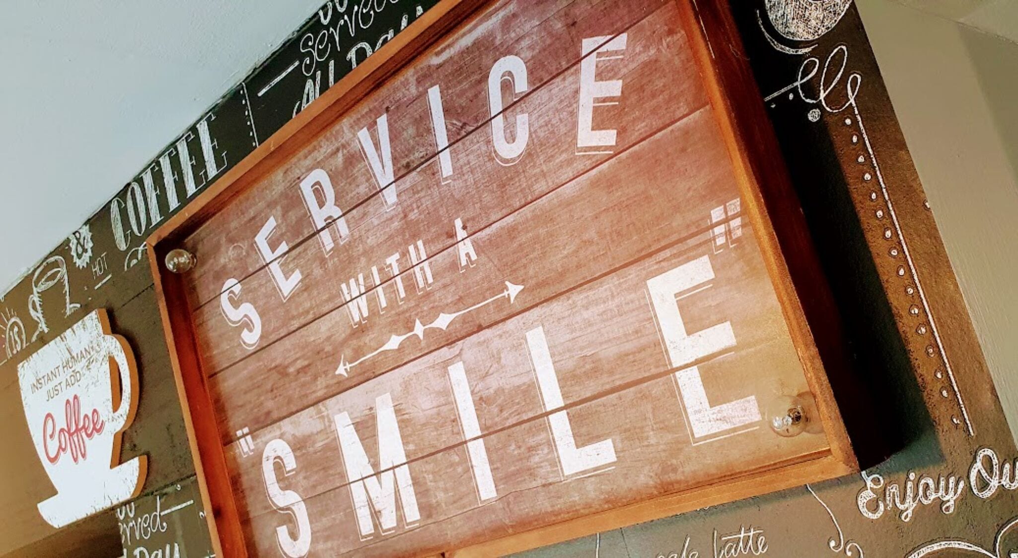 A wooden sign with the words "SERVICE WITH A SMILE" and a coffee cup illustration.