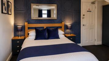 A neatly made bed with a wooden headboard, two bedside tables with lamps, a mirror above the bed, and a door to the right.
