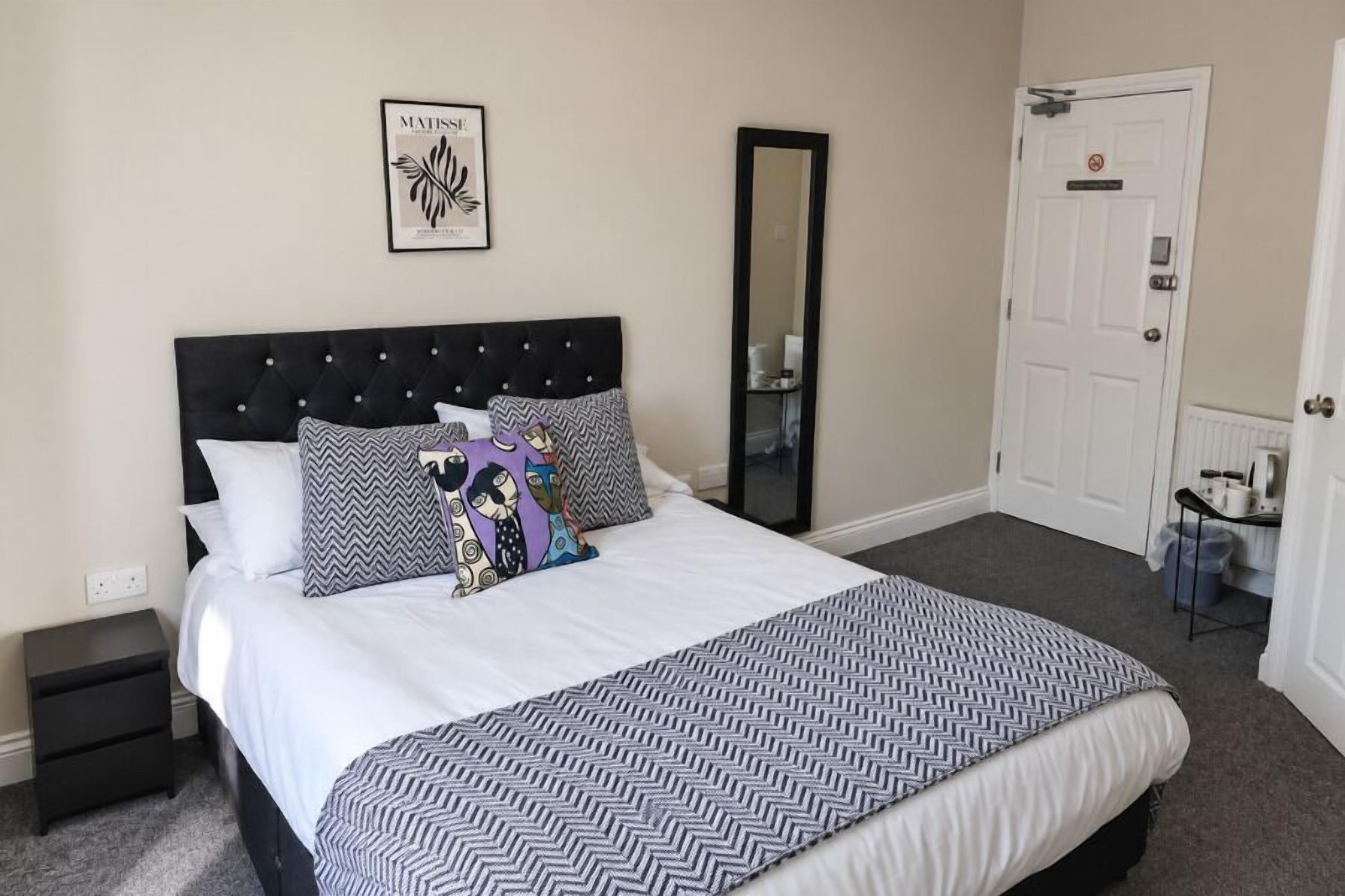 Uma cama bem arrumada com roupa de cama estampada, uma cabeceira preta e uma obra de arte emoldurada na parede.