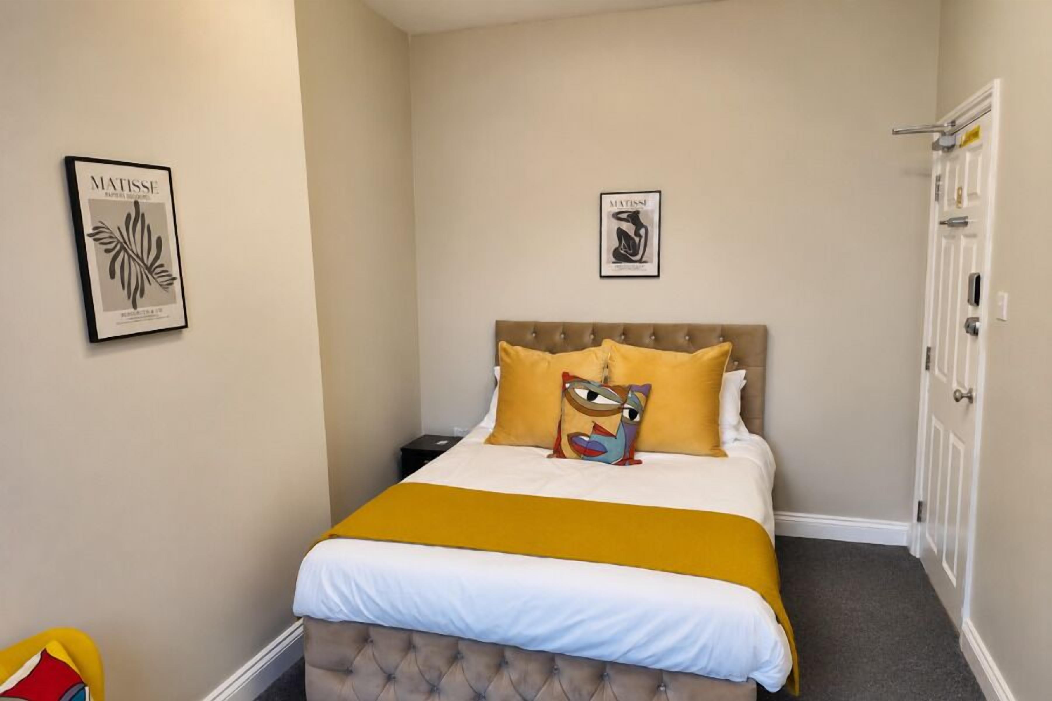 A neatly arranged bedroom with a bed, a nightstand, and two framed artworks on the wall.