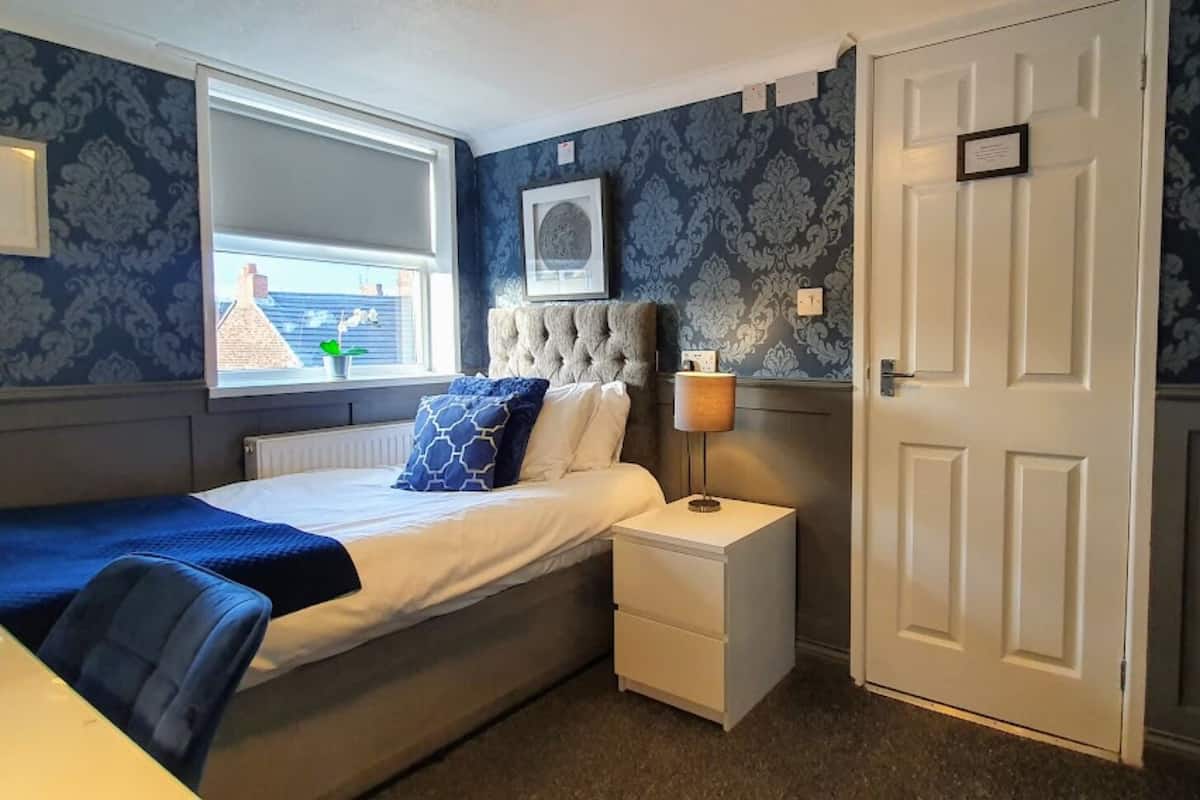 Un dormitorio con cama, mesita de noche, lámpara y ventana.