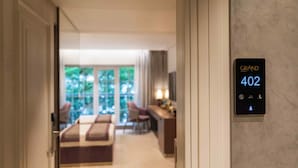A hotel room with a bed, a desk, and a view of greenery outside.