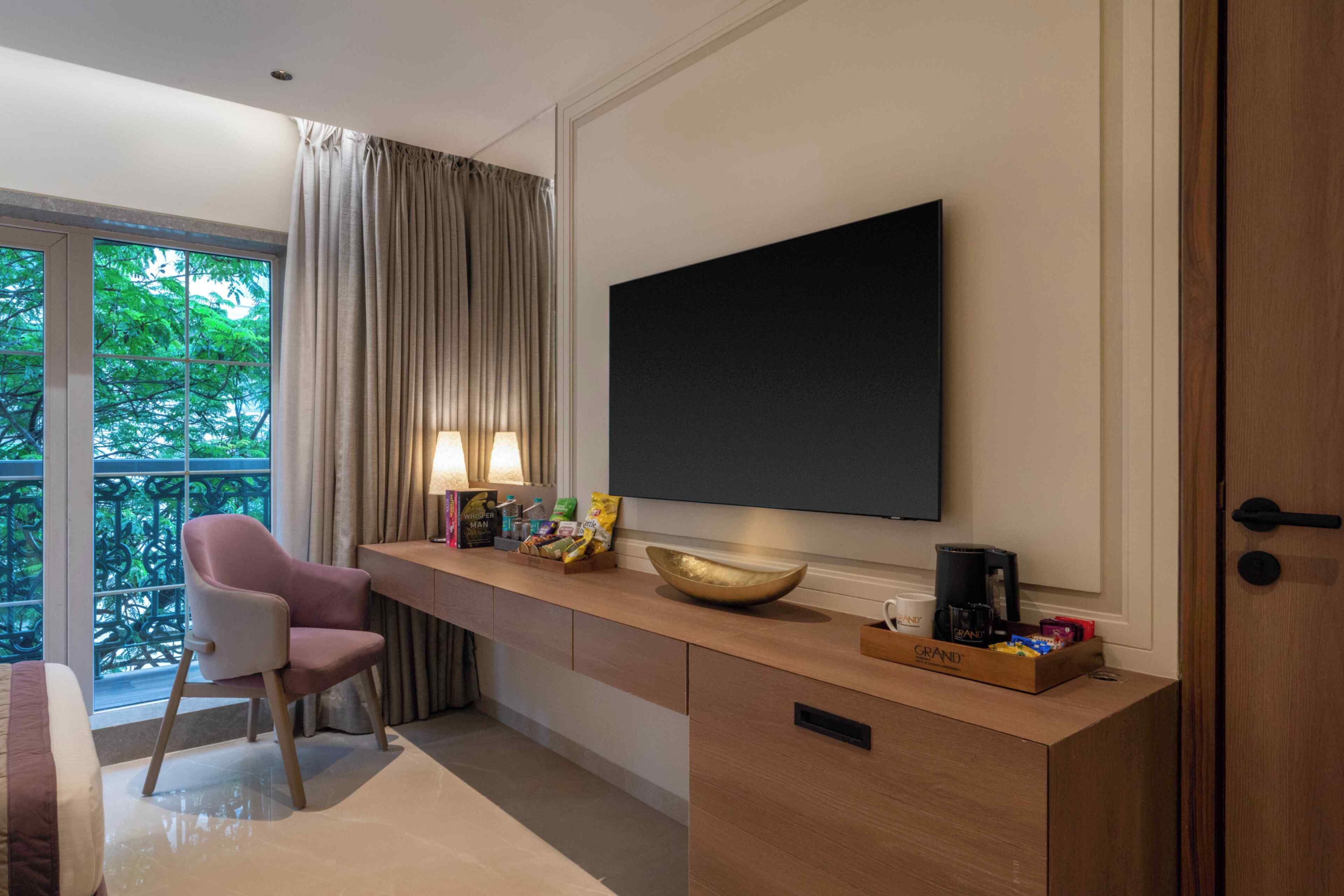 Habitación de hotel moderna con un ventanal grande, un escritorio con una computadora portátil, una silla, un televisor de pantalla plana y una cafetera.