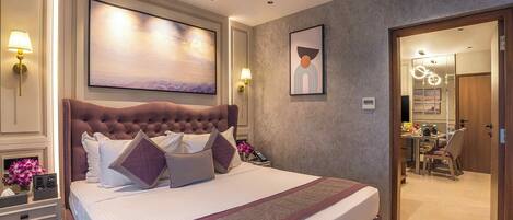 A bedroom with a large bed, bedside lamps, a painting, and a view into the bathroom.