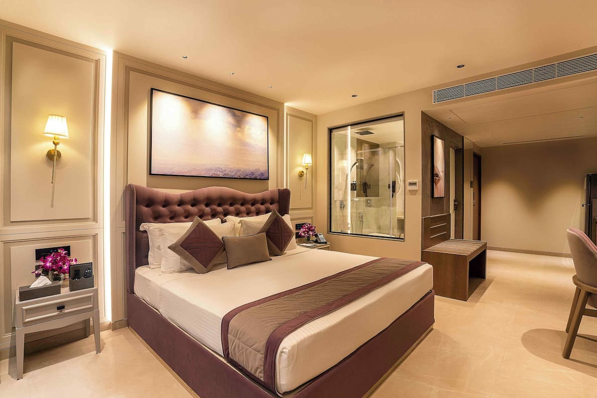 Habitación de hotel con una cama grande, lámparas de noche, un cuadro, un espejo, una mesita y una silla.