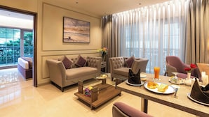 A modern hotel room with a sofa, armchairs, a dining table with breakfast, and a balcony with a view.