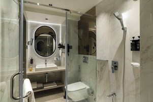 A modern bathroom with a glass-enclosed shower, a round mirror, a sink, and a toilet.