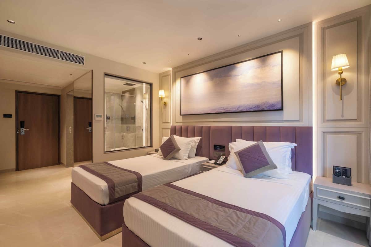 Habitación de hotel con dos camas, un espejo grande, un cuadro en la pared y una mesita de noche con lámpara.