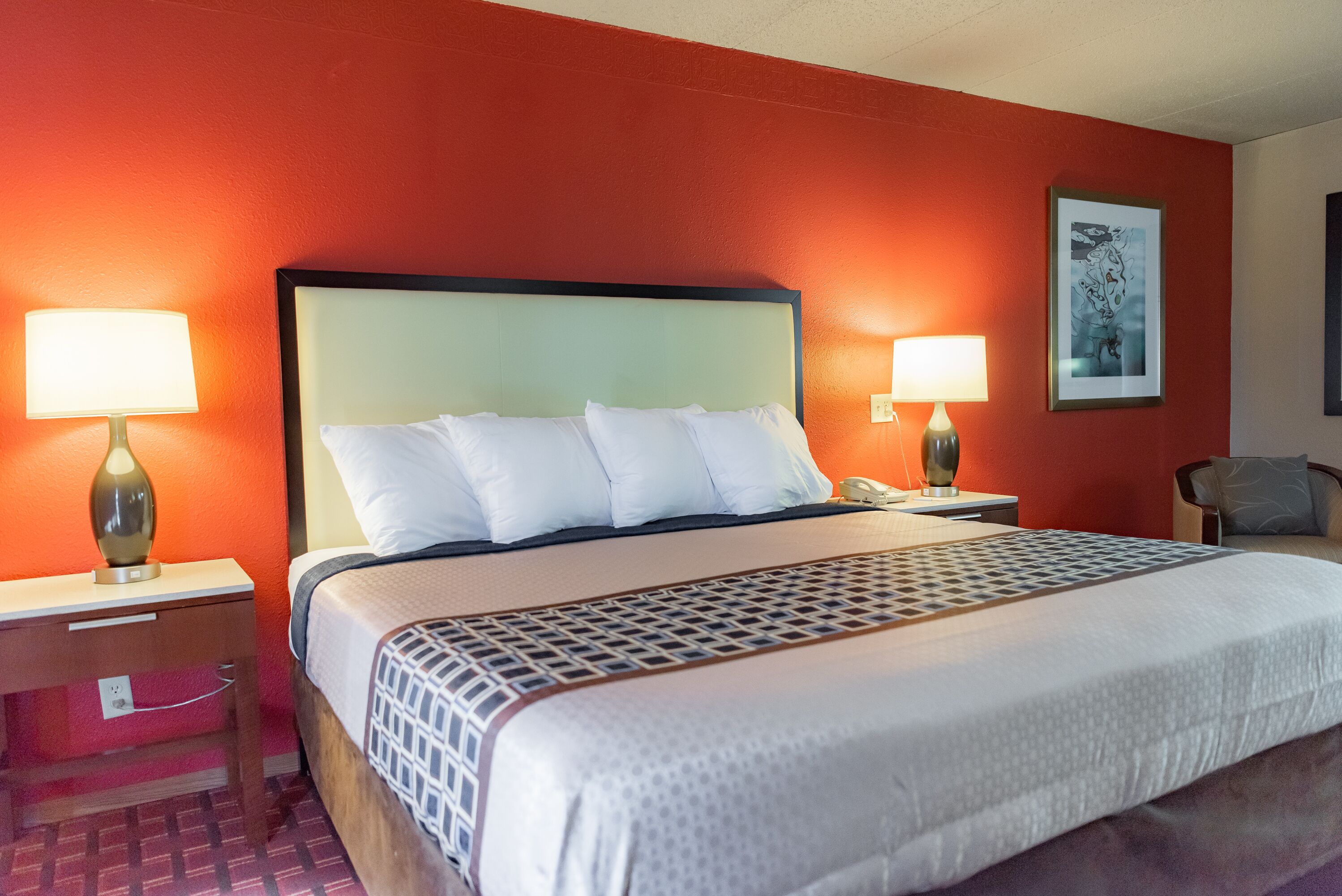 A hotel room with a bed, two bedside tables with lamps, a chair, and a framed picture on the wall.