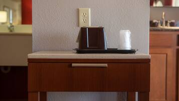 A small wooden table with a microwave and a cup on it, positioned against a wall with a power outlet.