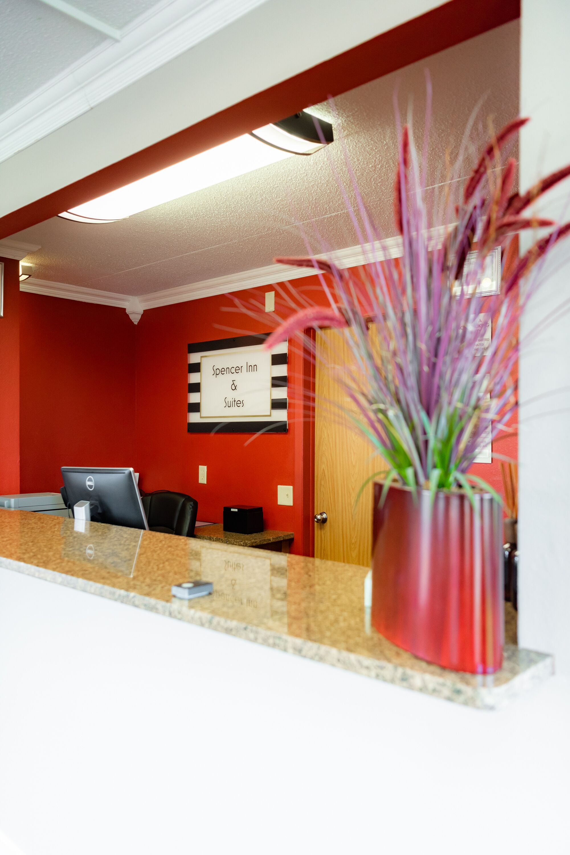 A reception desk with a computer, a potted plant, and a sign for Spencer Inn & Suites.