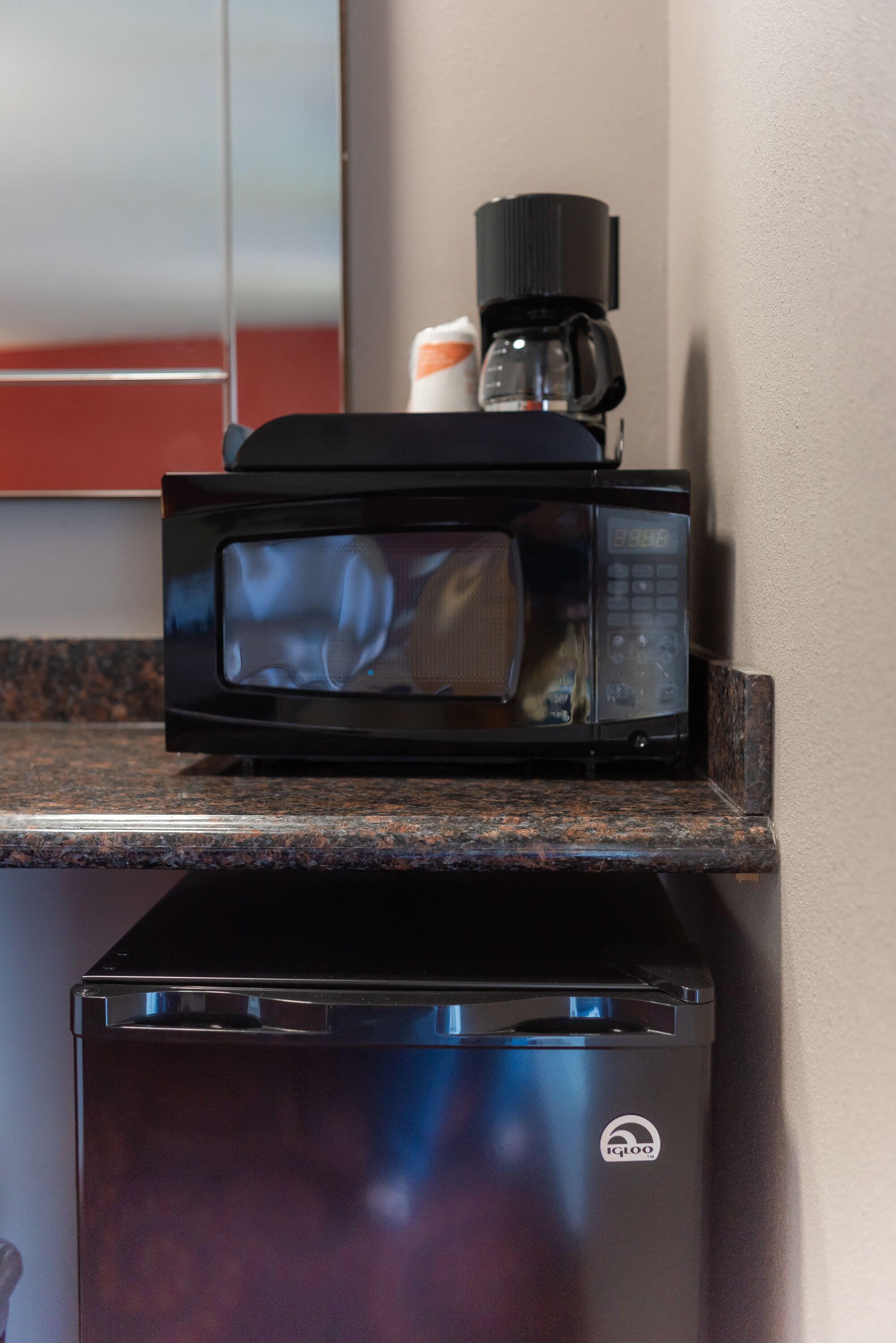A microwave on a granite countertop with a coffee maker and a small refrigerator below it.