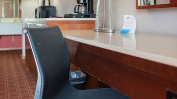 A hotel room with a desk, a chair, a lamp, a coffee maker, and a flat-screen TV.
