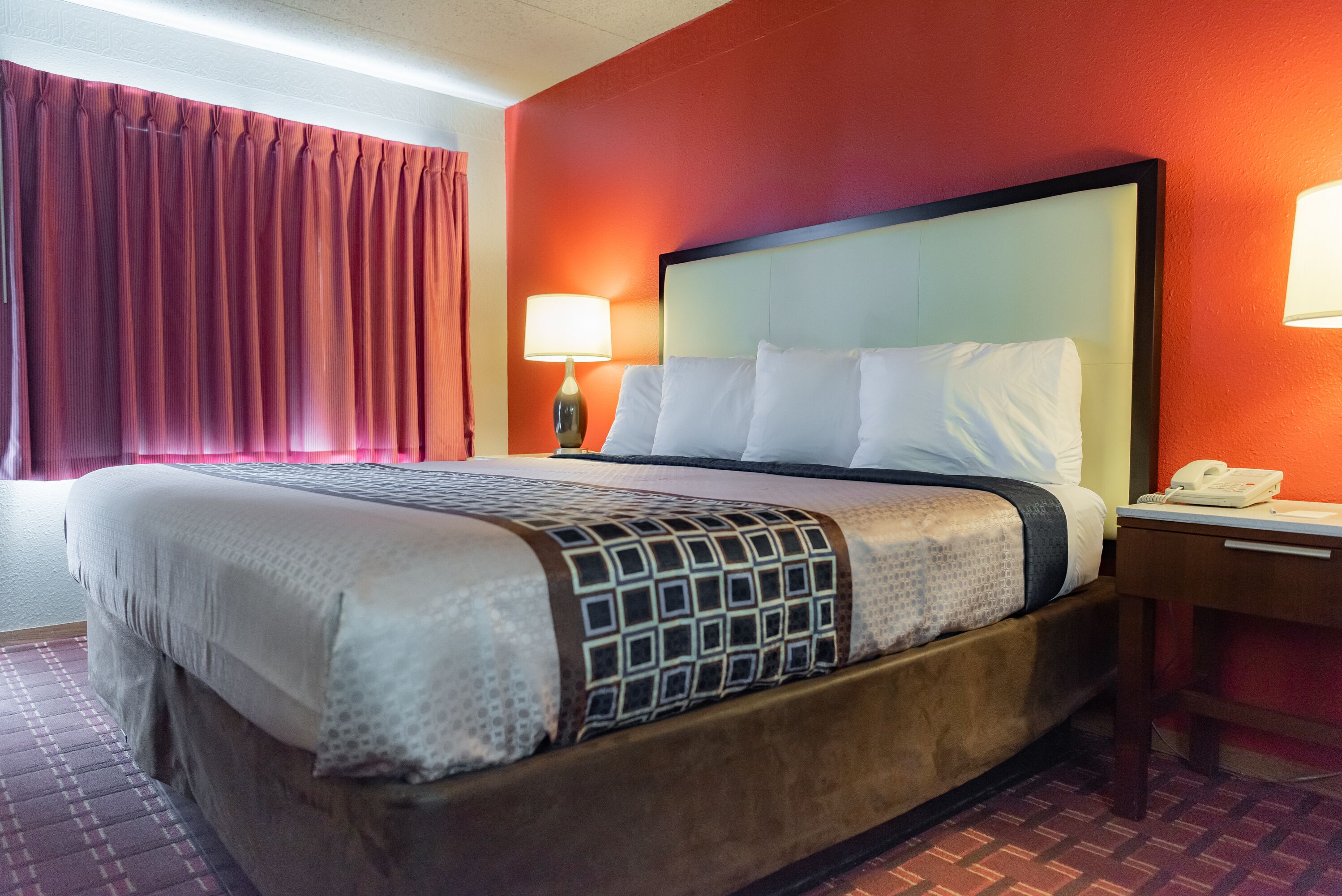 Habitación de hotel con una cama grande, una mesita de noche con lámpara y un teléfono.