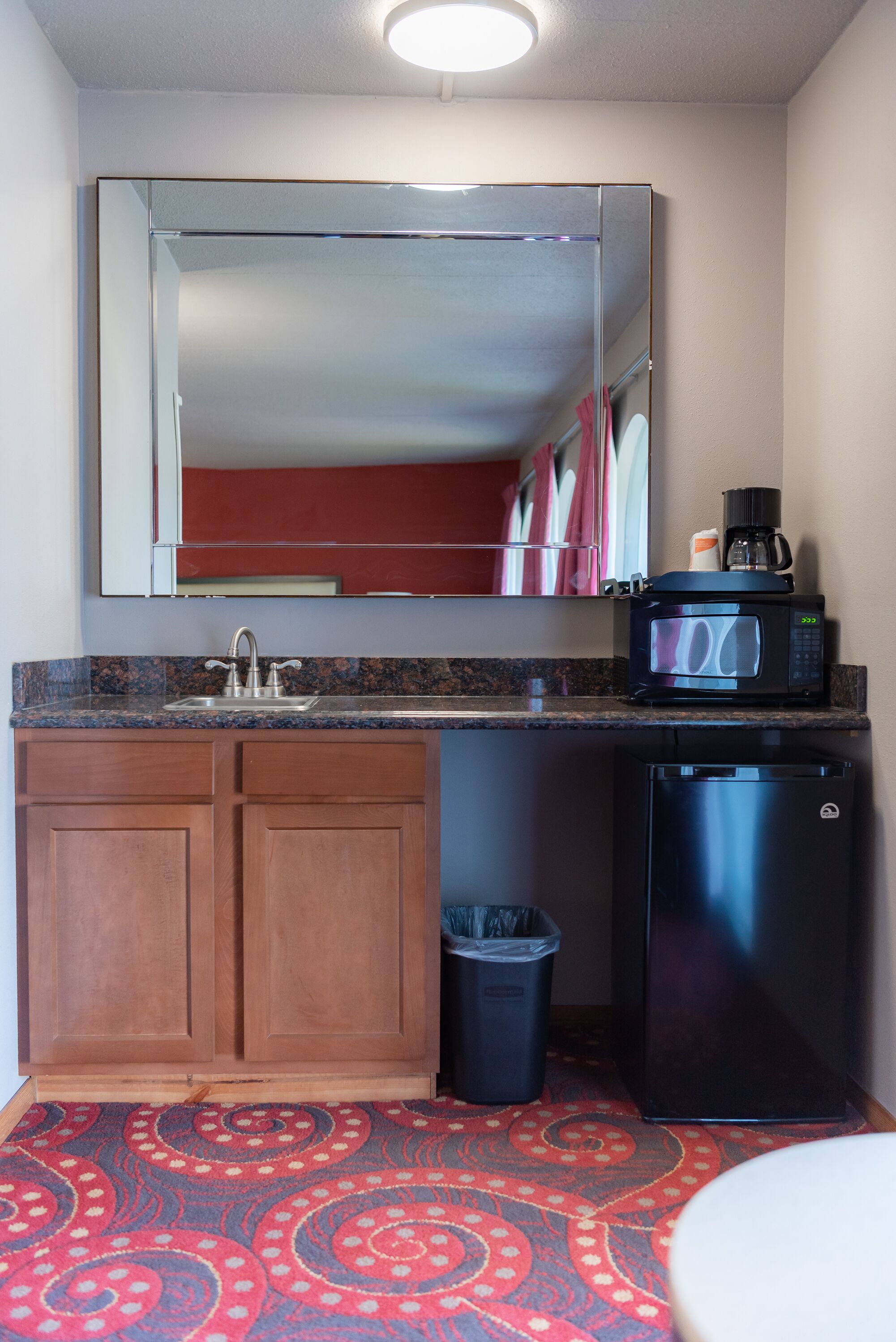 Una kitchenette compacta con microondas, cafetera y un bote de basura.