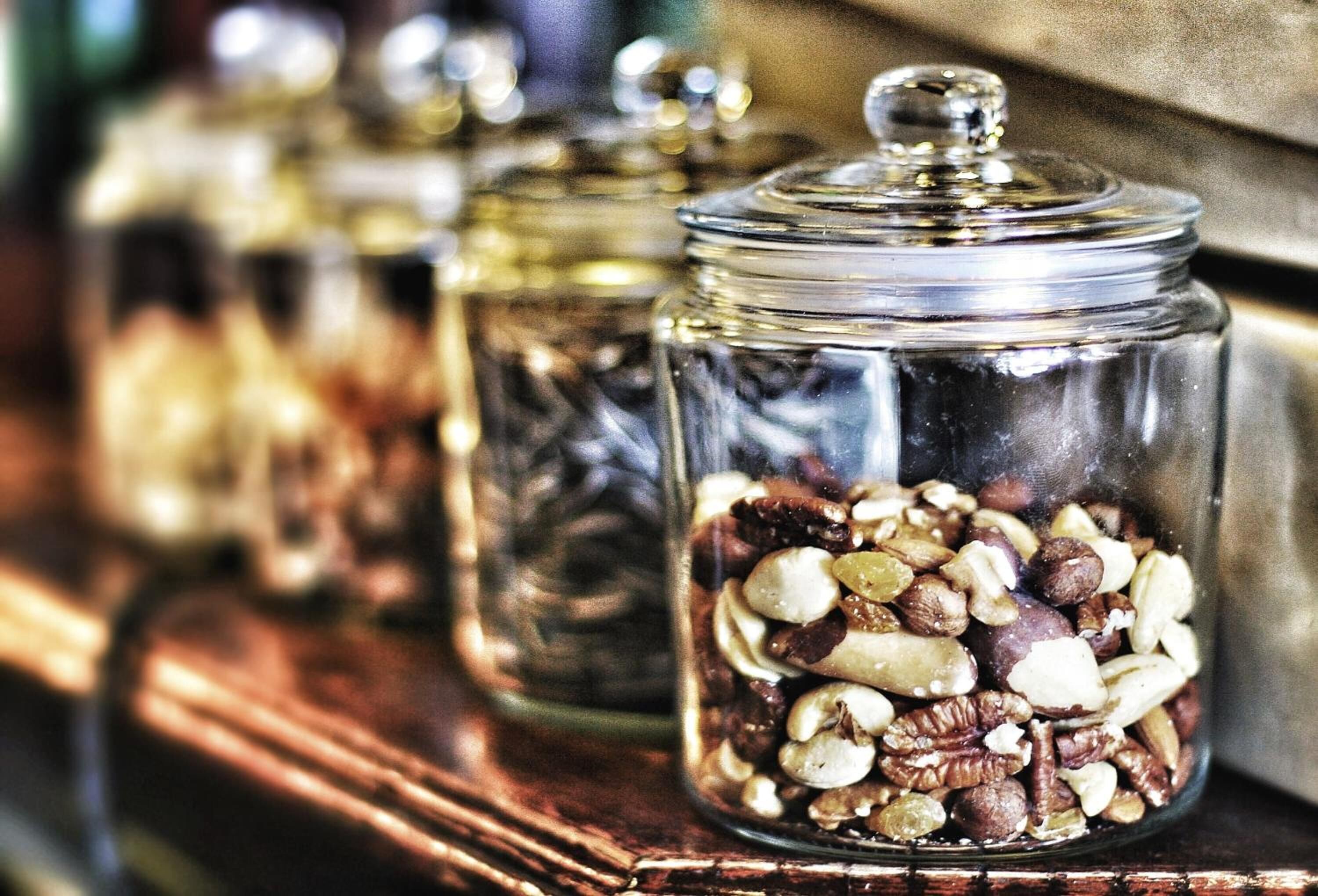 Glass jars filled with various nuts and seeds on a wooden shelf.