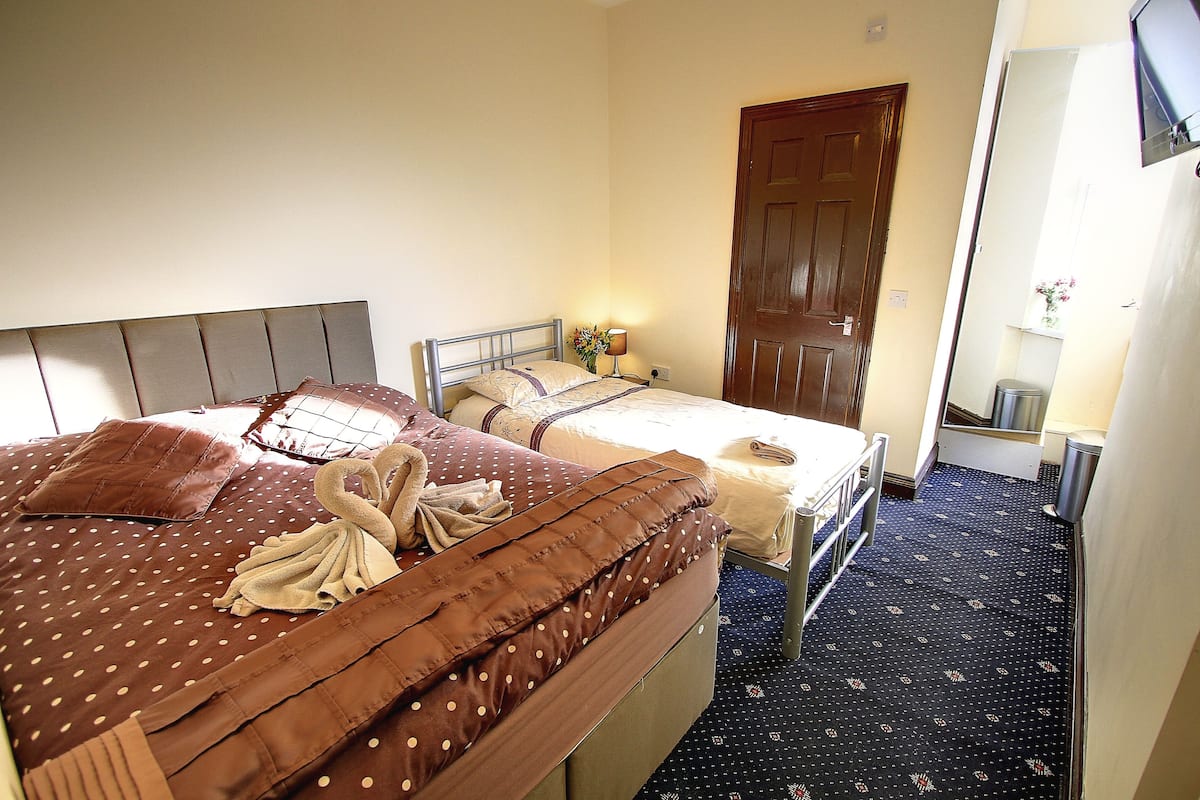A hotel room with two beds, a wooden door, a small table with a lamp, and a trash can.