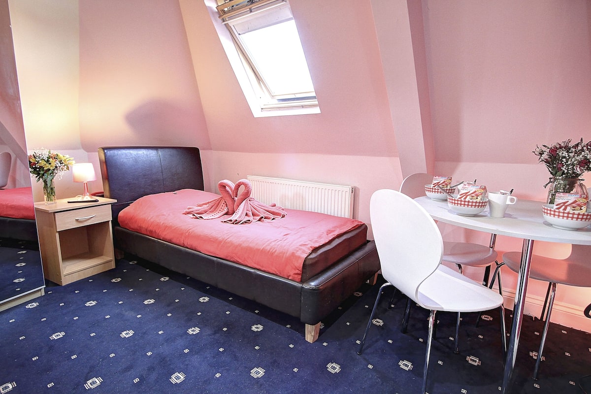 A hotel room with a bed, a desk, a chair, a lamp, and a window.