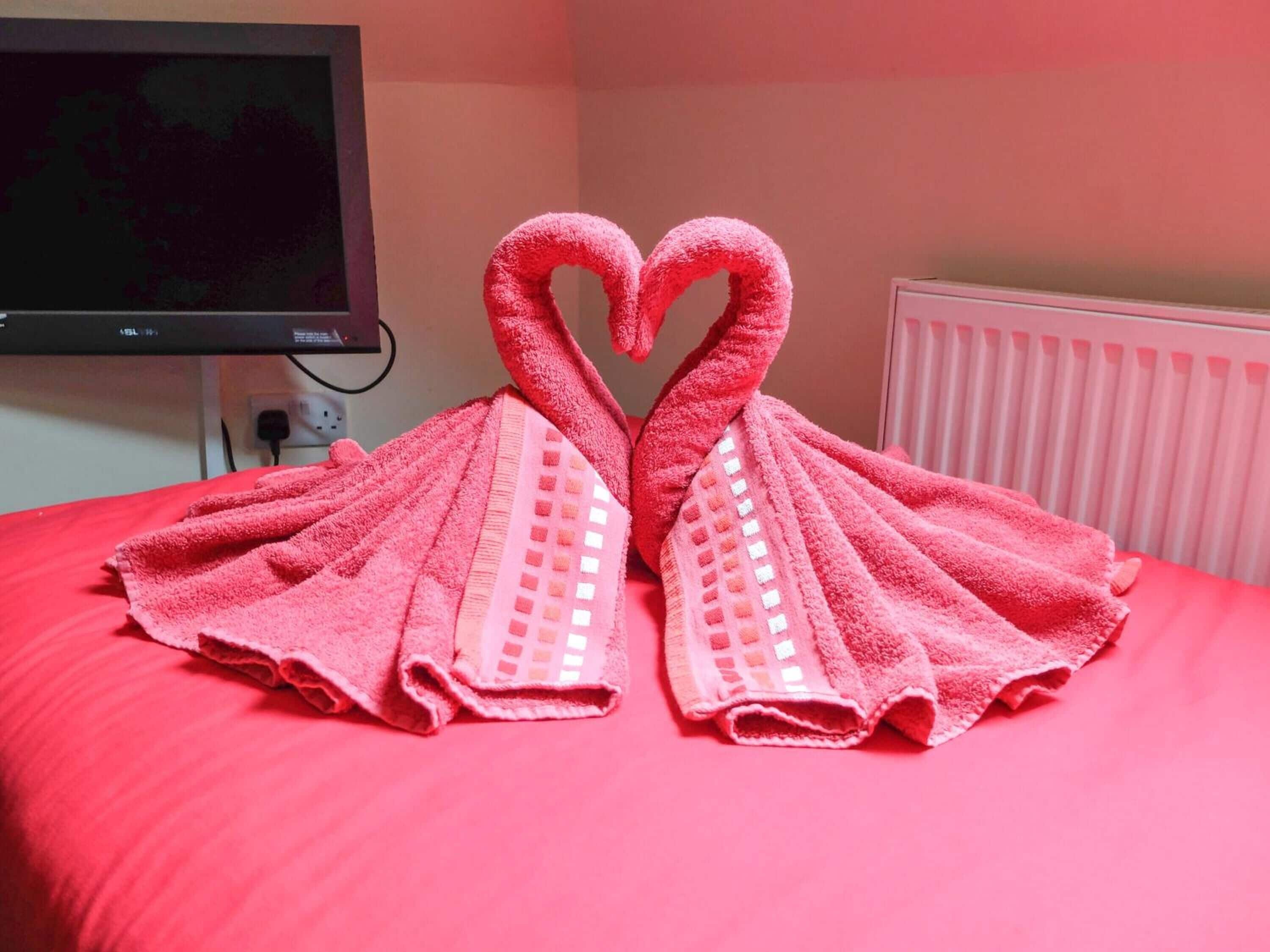 A bed with a red blanket and two towels arranged in the shape of swans.