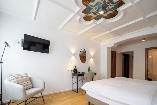 A modern hotel room with a bed, a desk, a chair, a flat-screen TV, and a ceiling with decorative molding.