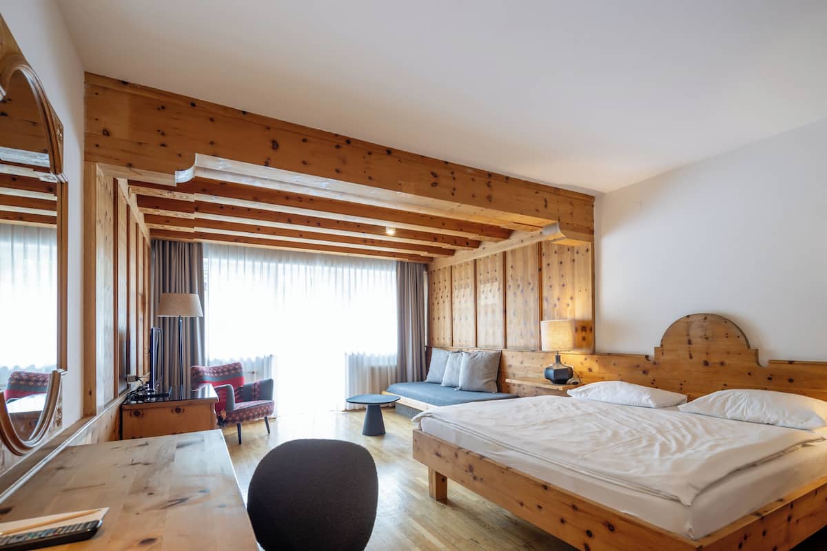A hotel room with a wooden ceiling, a bed, a sofa, a desk, and a chair.