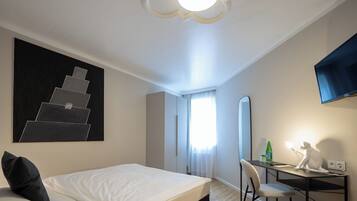 A hotel room with a bed, a desk, a chair, a flat-screen TV, a painting, and a staircase.