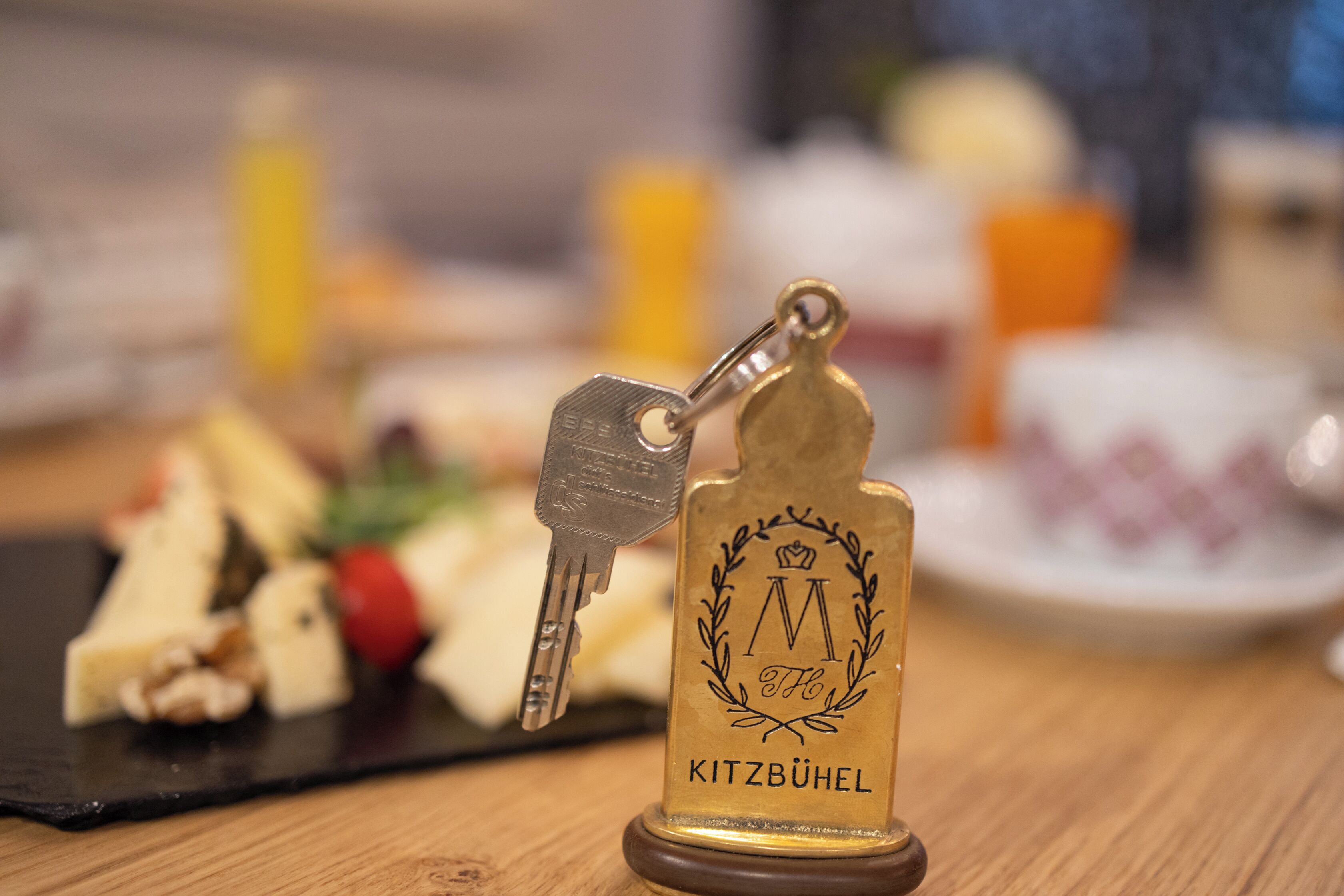 Un llavero con la inscripción "Kitzbühel" y una llave, sobre una superficie de madera con un fondo borroso de comida.