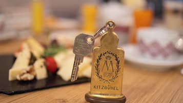 A keychain with the inscription "Kitzbühel" and a key, placed on a wooden surface with a blurred background of food items.