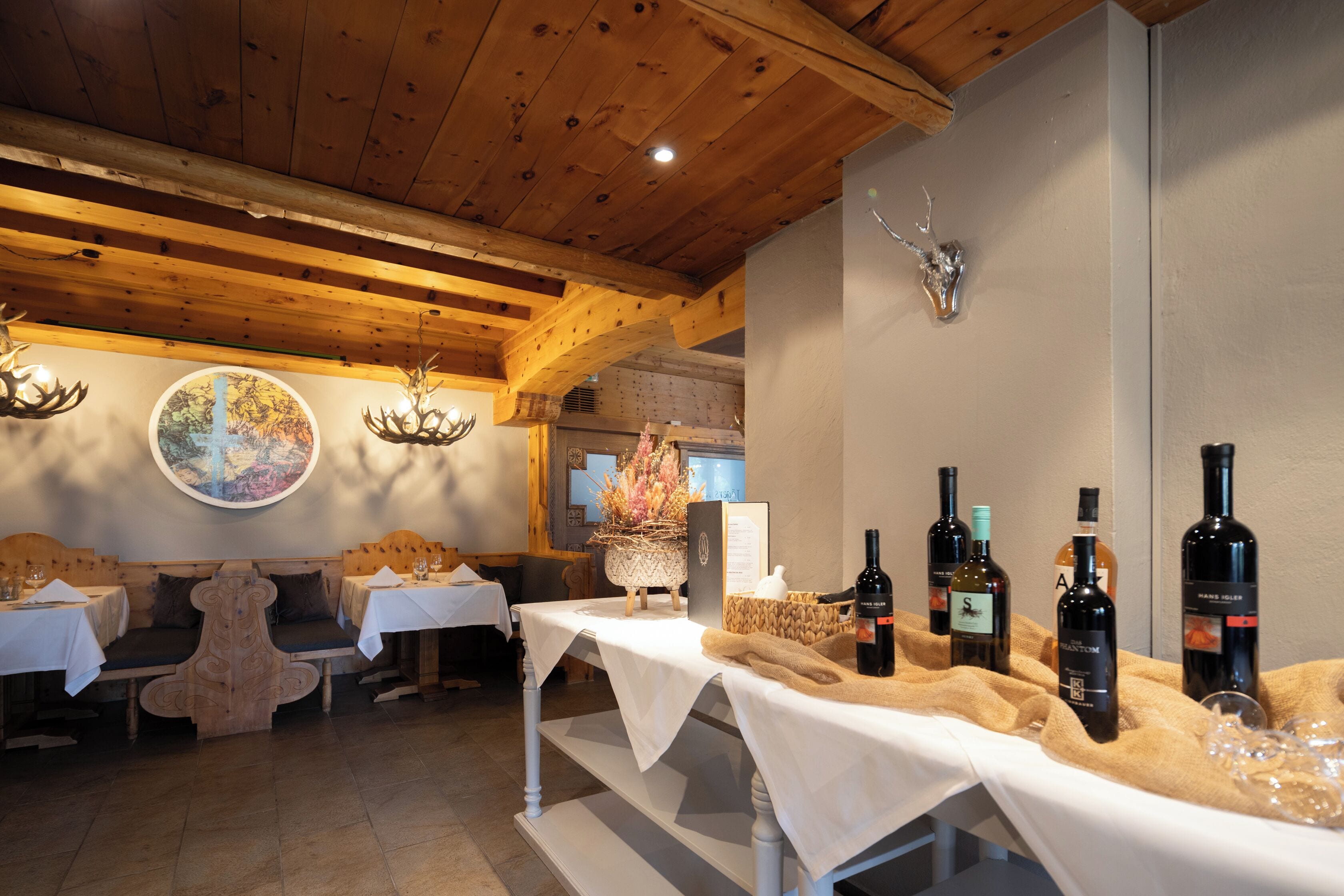 Un restaurante con vigas de madera, mesas redondas y un adorno de cabeza de ciervo en la pared.